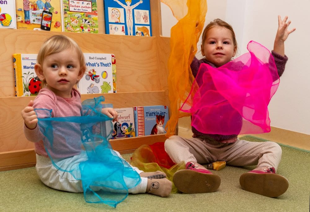 Zwei Kleinkinder spielen mit bunten Tüchern.
