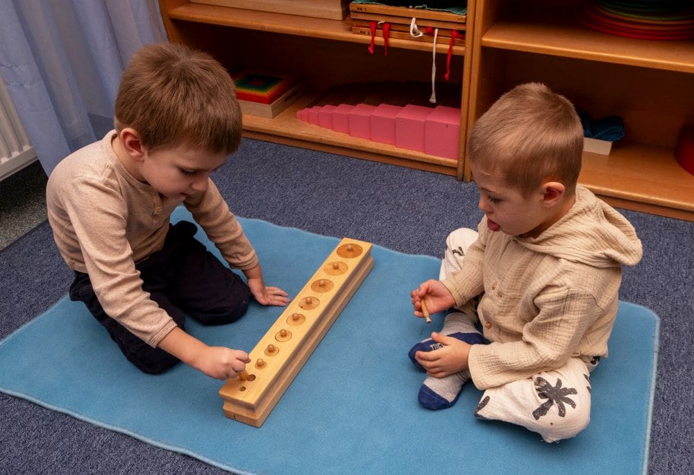 Zwei Kinder sortieren unterschiedlich große Stäbe in dafür vorgesehene Löcher in einem Holzbrett.
