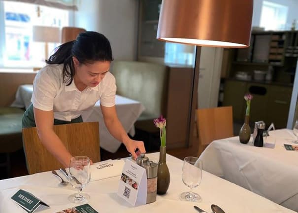 Eine junge Frau deckt einen eleganten Tisch. Sie macht ein Praktikum in einem Gastronomiebetrieb.