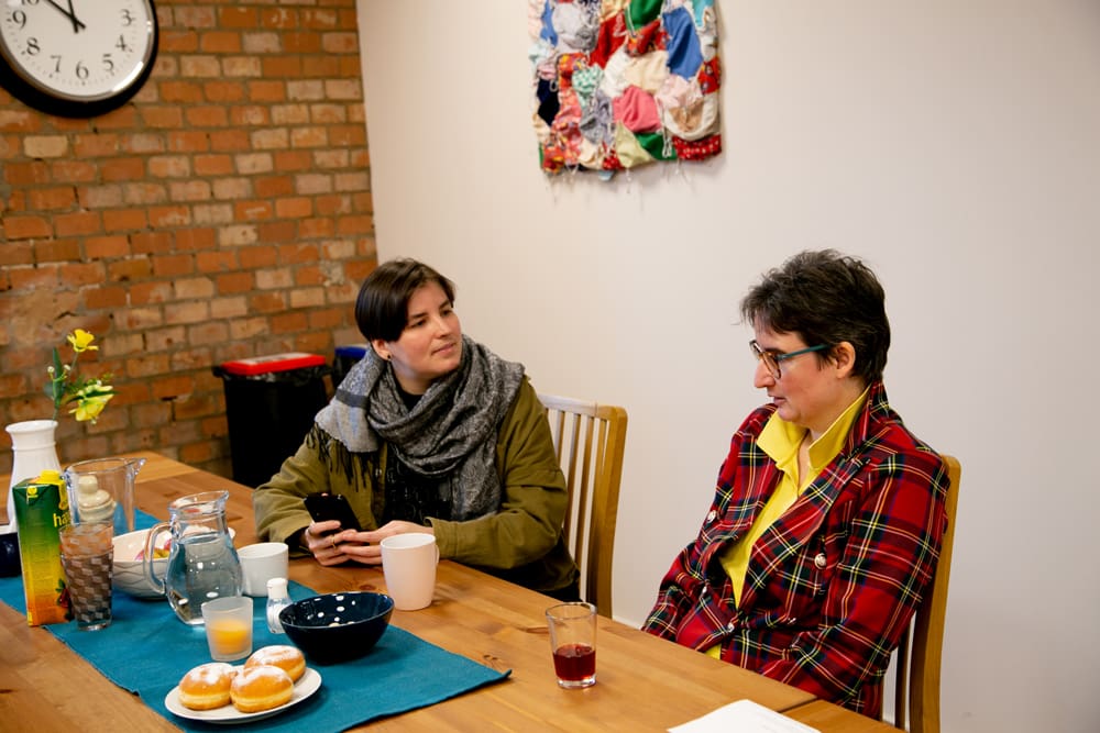 Eine Klientin und eine Mitarbeiterin von KoMiT sitzen gemeinsam am Tisch und unterhalten sich. Sie sind an einem Stützpunkt für teilbetreutes Wohnen in Wien.