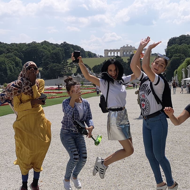 Vier Teilnehmerinnen und eine Mitarbeiterin von bildung.bewegt Mädchen NBS sind gemeinsam im Schlosspark von Schönbrunn in Wien. Sie lachen und springen in die Luft.