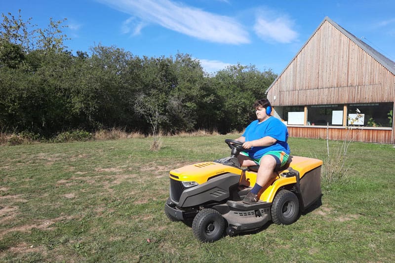 Ein Schüler der FIT-Schule der ITA Gänserndorf fährt auf einem Sitzrasenmäher über eine Wiese vom Öko-Landgut Sonnenfeld.